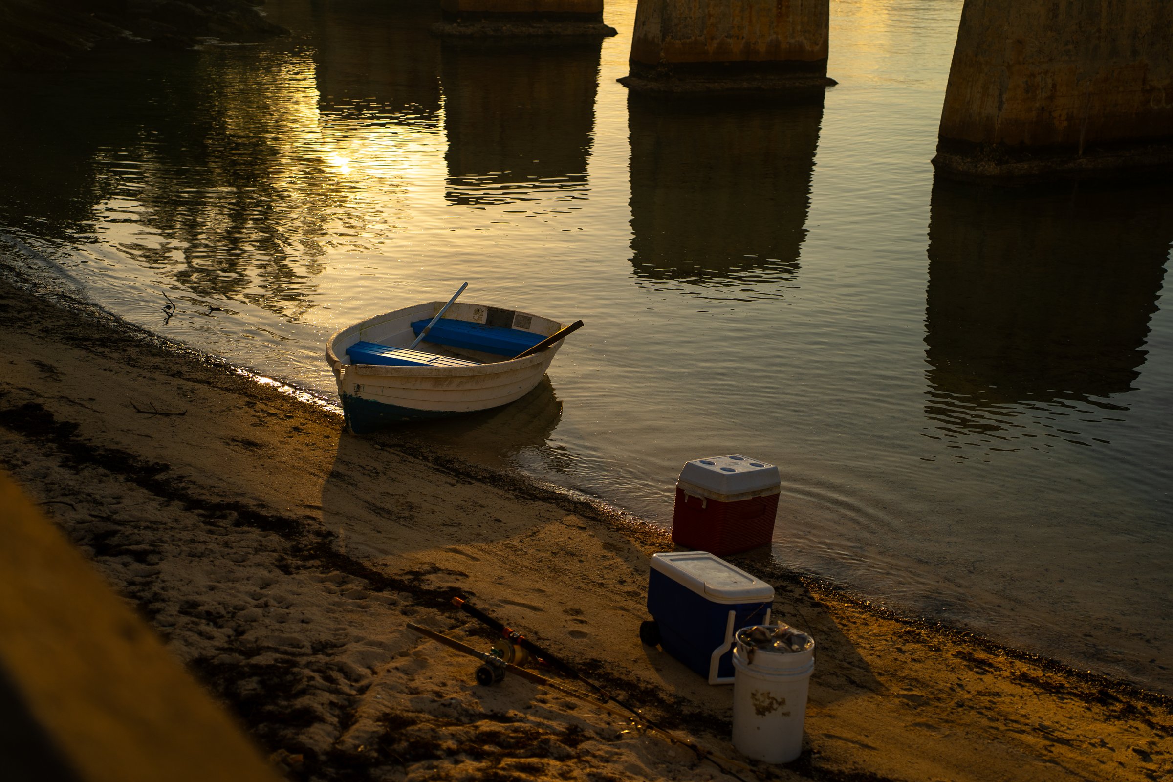Fishing boat on shore at golden hour under bridge piers
